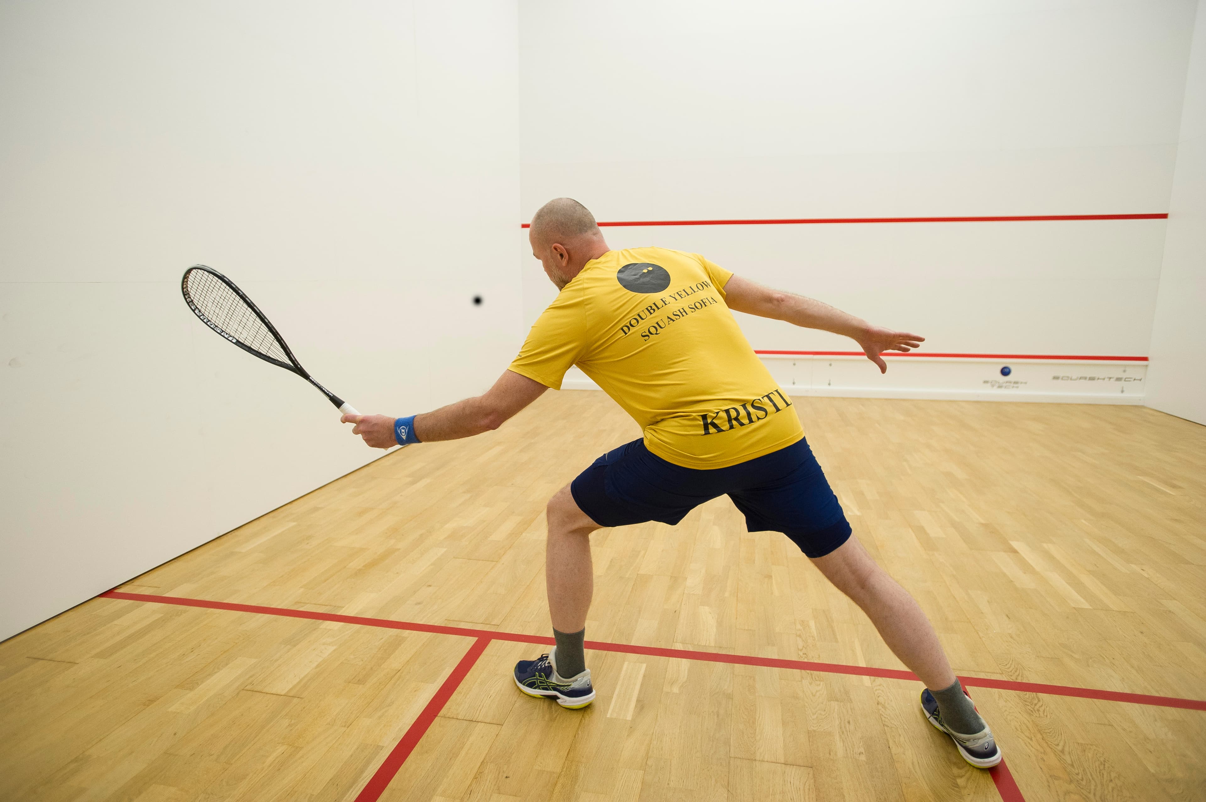 Professional squash player serving on a bright, newly renovated court